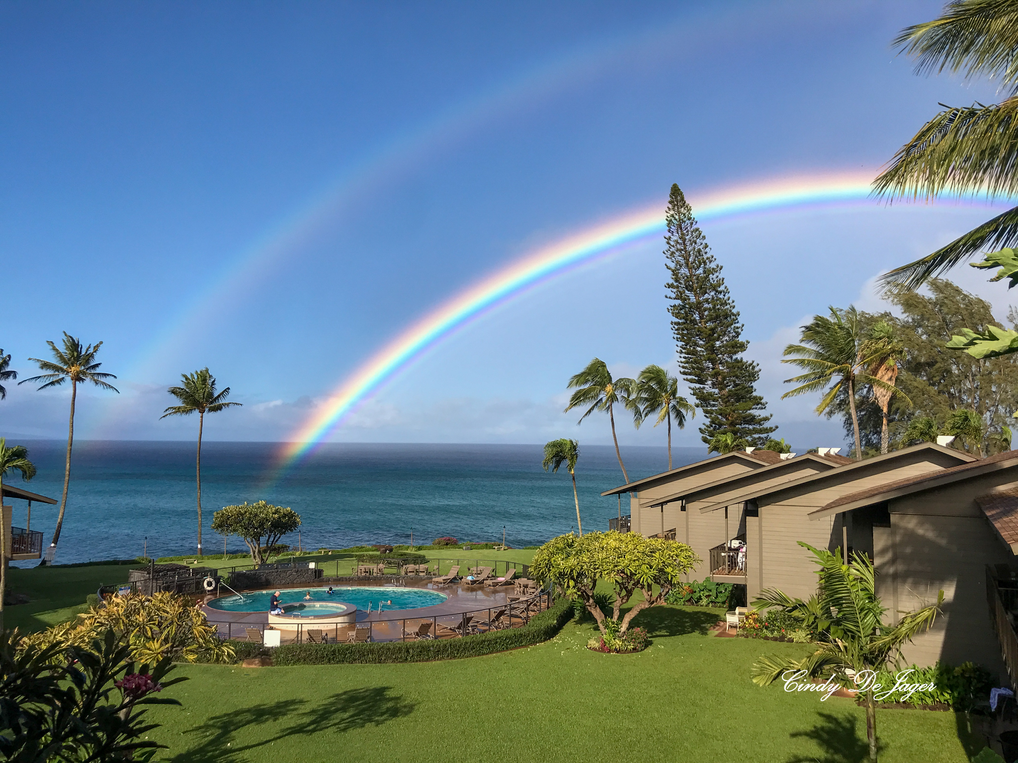 A double rainbow over a Maui resort on the ocean. The ends of the rainbow appear to be dissolving into the blueness of the ocean.